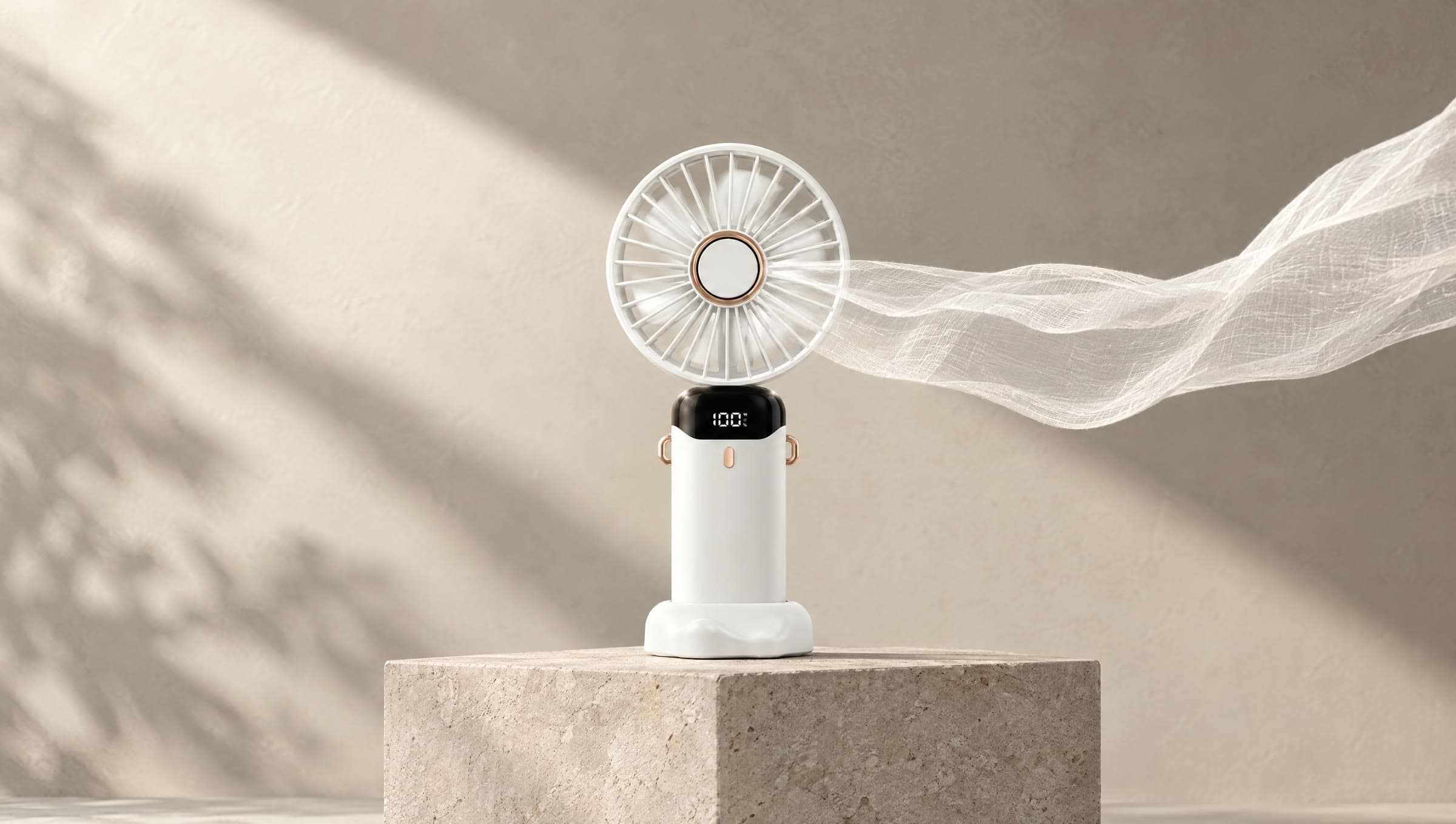 Mini ventilador branco ligado sobre um bloco de pedra, com um tecido leve levado pelo vento
